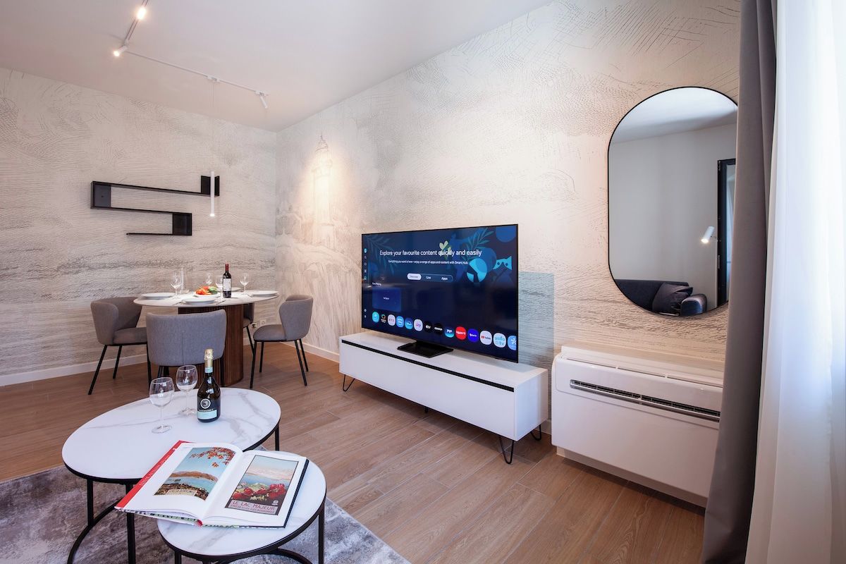 A modern living room with a flat-screen TV, a dining table, chairs, a magazine, and a large mirror.