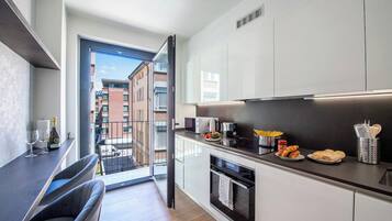 A modern kitchen with a sliding door to a balcony, a dining area with chairs, and a counter with food items.