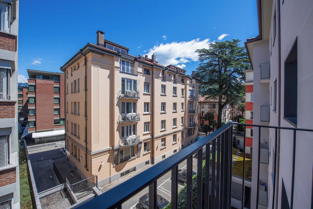 A multi-story residential building with balconies, a clear sky, and a tree in the background.