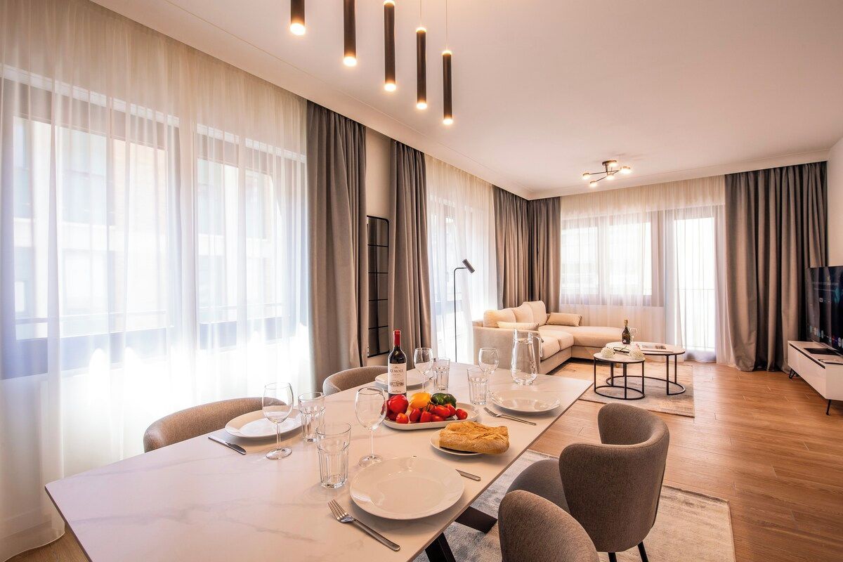 A modern hotel room with a dining area, a sofa, and a television.