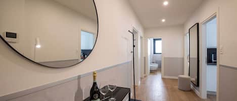 Un couloir moderne avec un grand miroir, une console noire sur laquelle sont posés une bouteille et des verres, et un luminaire.