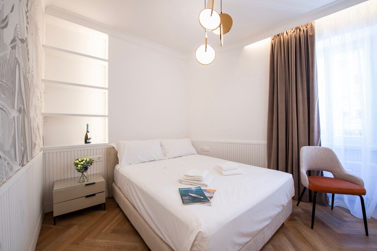 Una habitación de hotel con una cama grande, una mesita de noche, una silla y un estante en la pared.