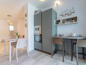 Eine moderne Küche mit Einbauofen, Essbereich mit Tisch und Stühlen sowie ein Regal mit Gläsern.