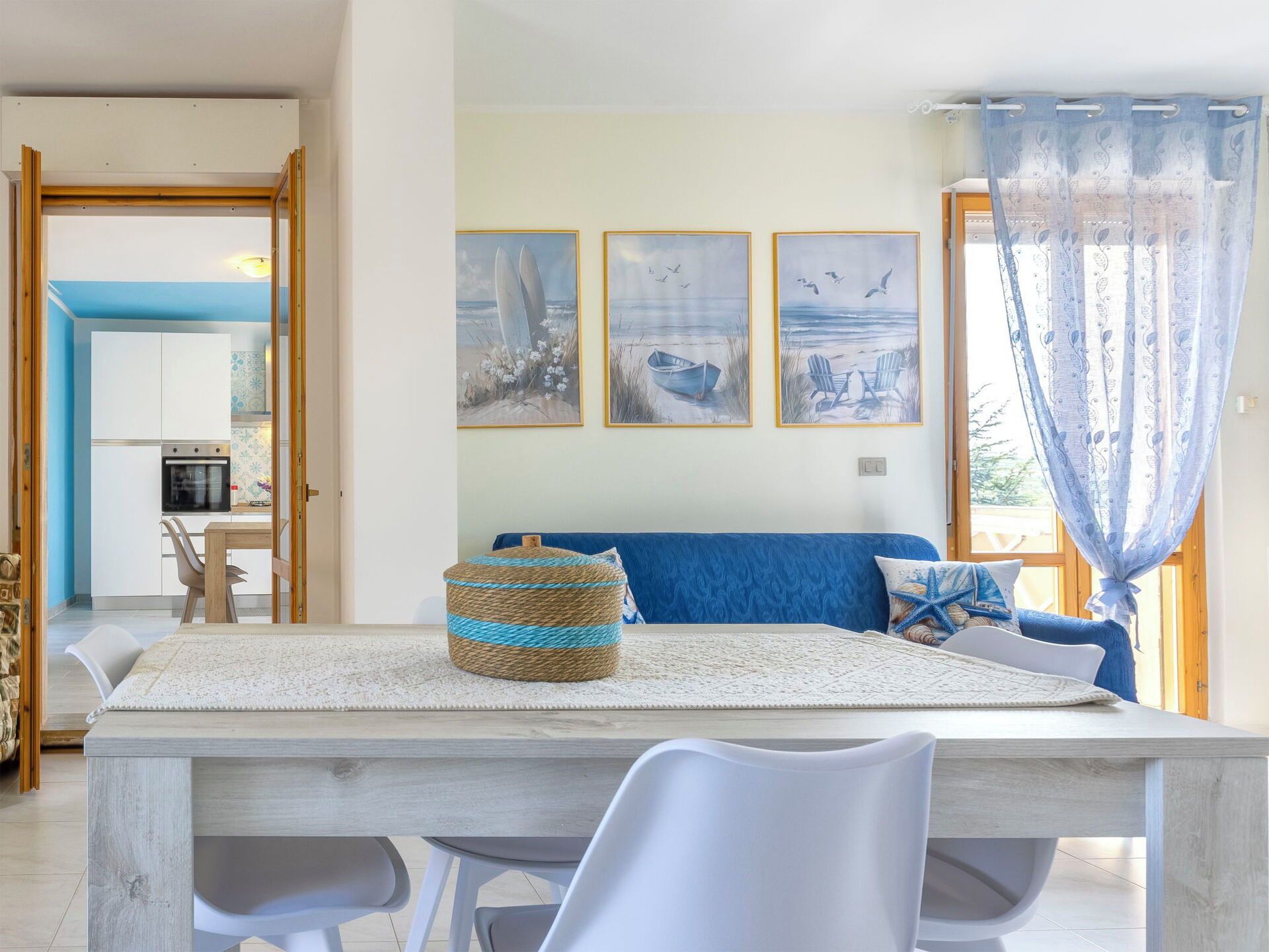 A dining area with a wooden table, white chairs, and a blue sofa with a nautical-themed pillow.