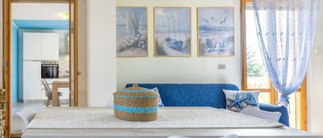 A dining area with a wooden table, white chairs, and a blue sofa with a nautical-themed pillow.