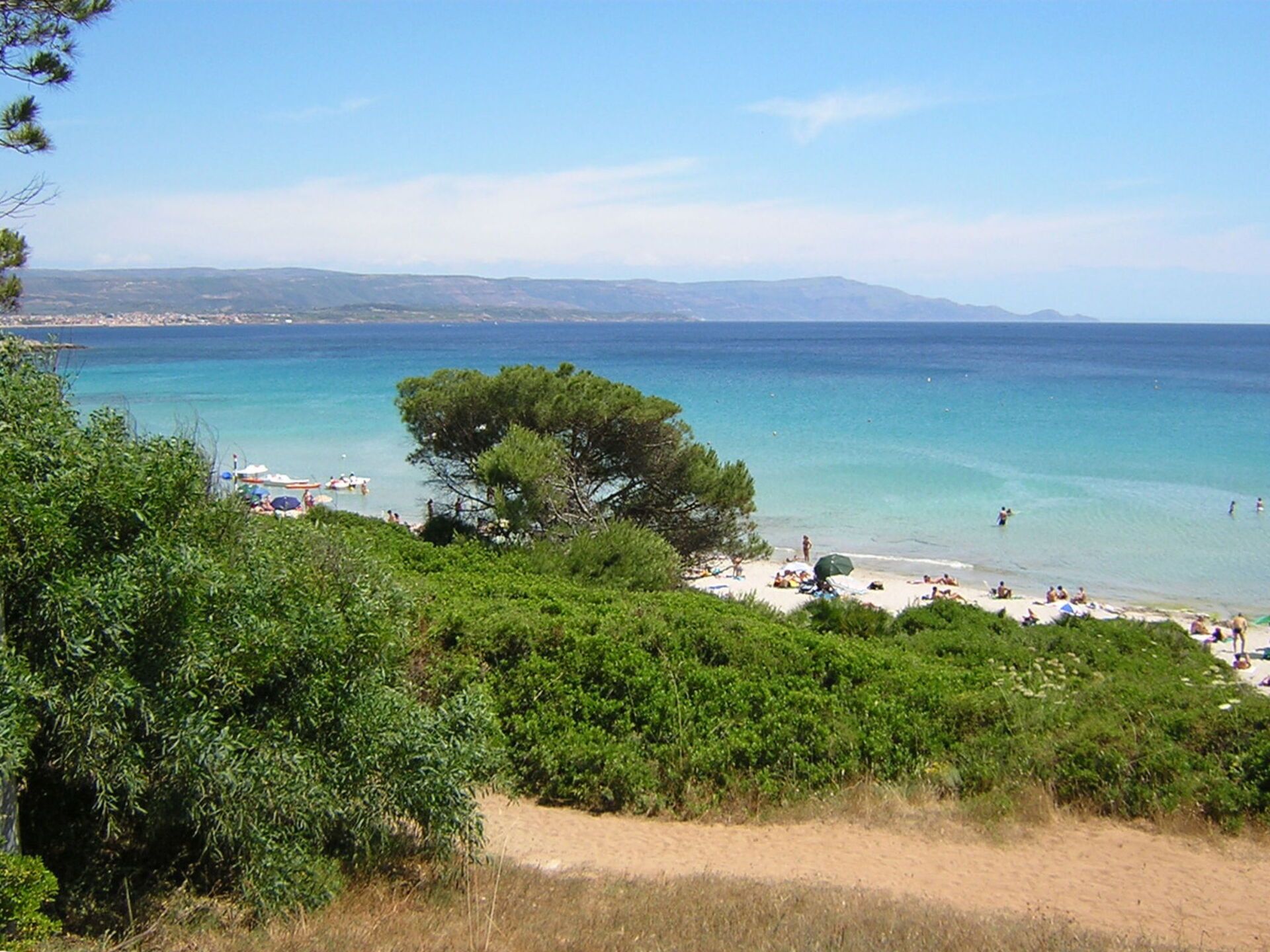 Uma praia com águas turquesa cristalinas, uma faixa de areia e algumas pessoas aproveitando o sol.