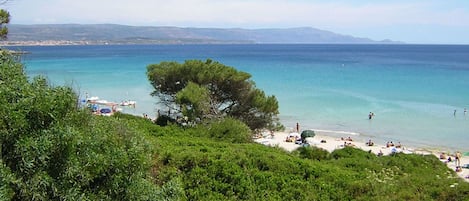 A beach with clear turquoise water, a sandy shore, and a few people enjoying the sun.