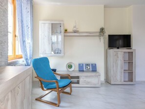 A living room with a wooden rocking chair, a television on a cabinet, and a decorative shelf with items. - Nice apartment for 6 people with WIFI, A/C, TV and patio (Alghero)