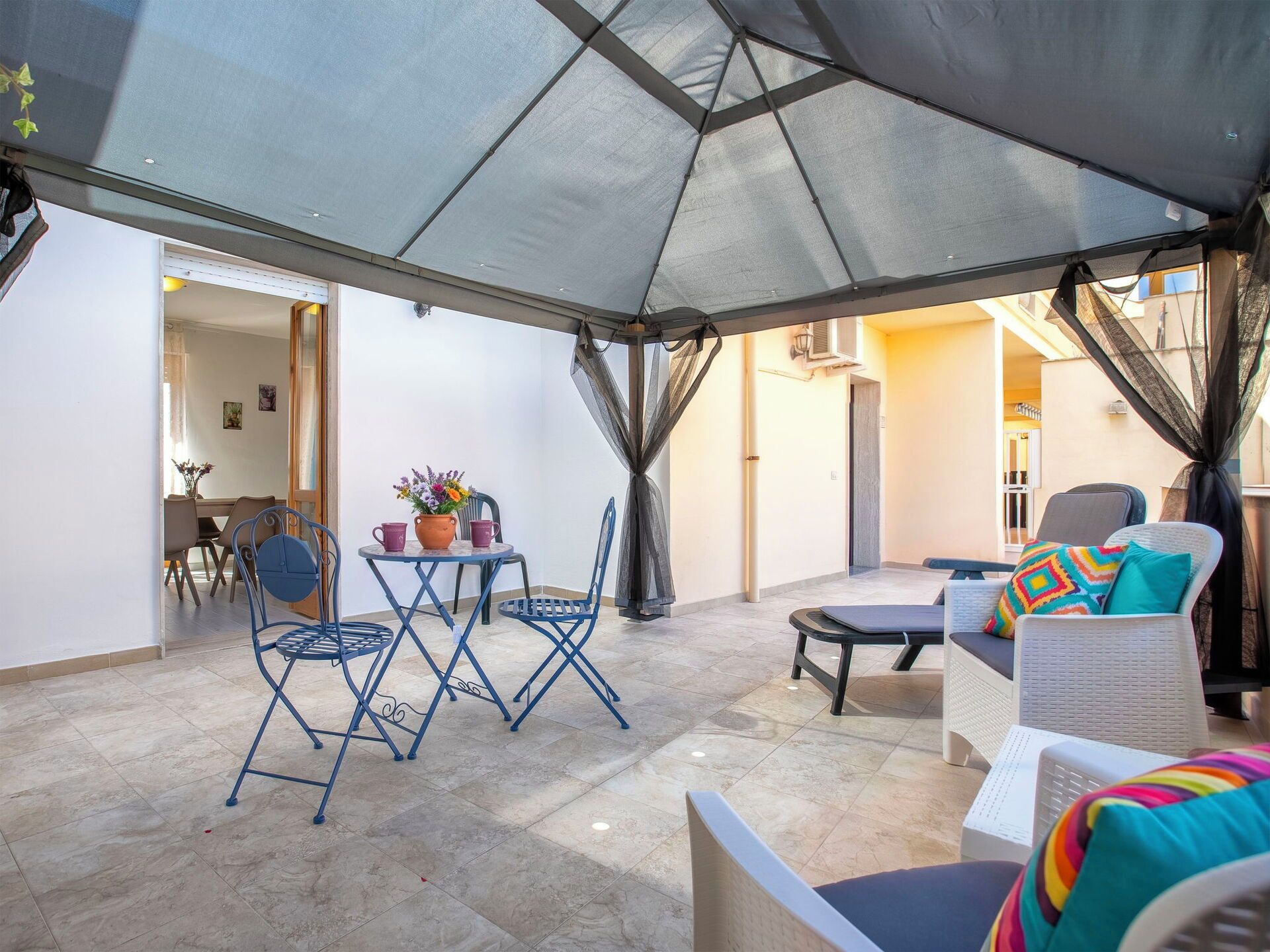 Een buitenpatio met een tafel en stoelen, een overdekte zithoek en uitzicht op het interieur.