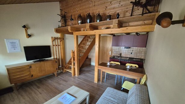 A cozy living room with a wooden staircase, a dining area, and a kitchen with a tiled backsplash. - Small, Cozy Apartment with Country Charm, Shared Garden & Wi-Fi (FeWo 4) (Hörselberg-Hainich)