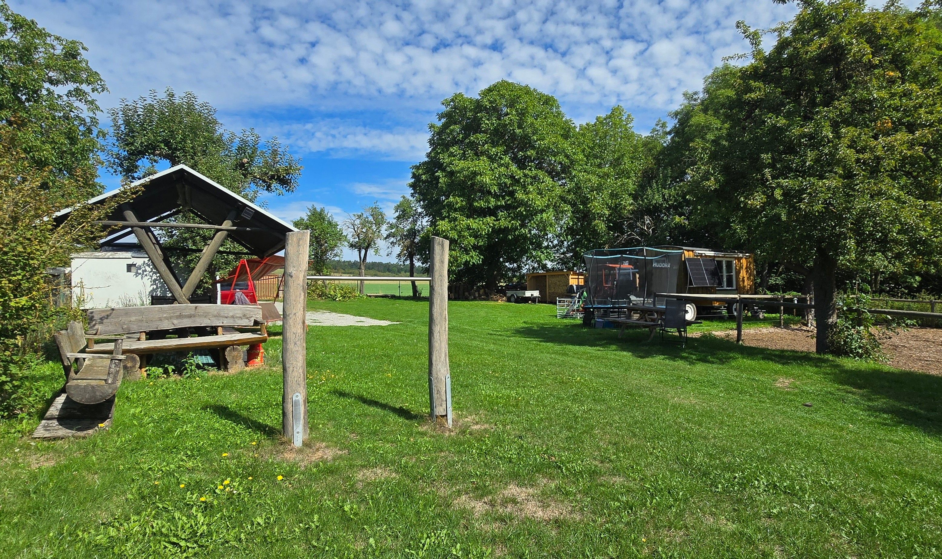 A rustic outdoor setting with a wooden structure, a covered area, and a vehicle.