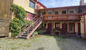 A courtyard with cobblestone paving, a wooden staircase, and a building with multiple windows and doors. - Small, Cozy Apartment with Country Charm, Shared Garden & Wi-Fi (FeWo 4) (Hörselberg-Hainich)