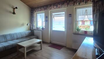 A living room with a wooden ceiling, a sofa, a coffee table, a television, and a window with curtains.