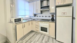 A kitchen with white cabinets, a microwave, a stove, and a refrigerator. - Puertas de la Catedral (Córdoba)