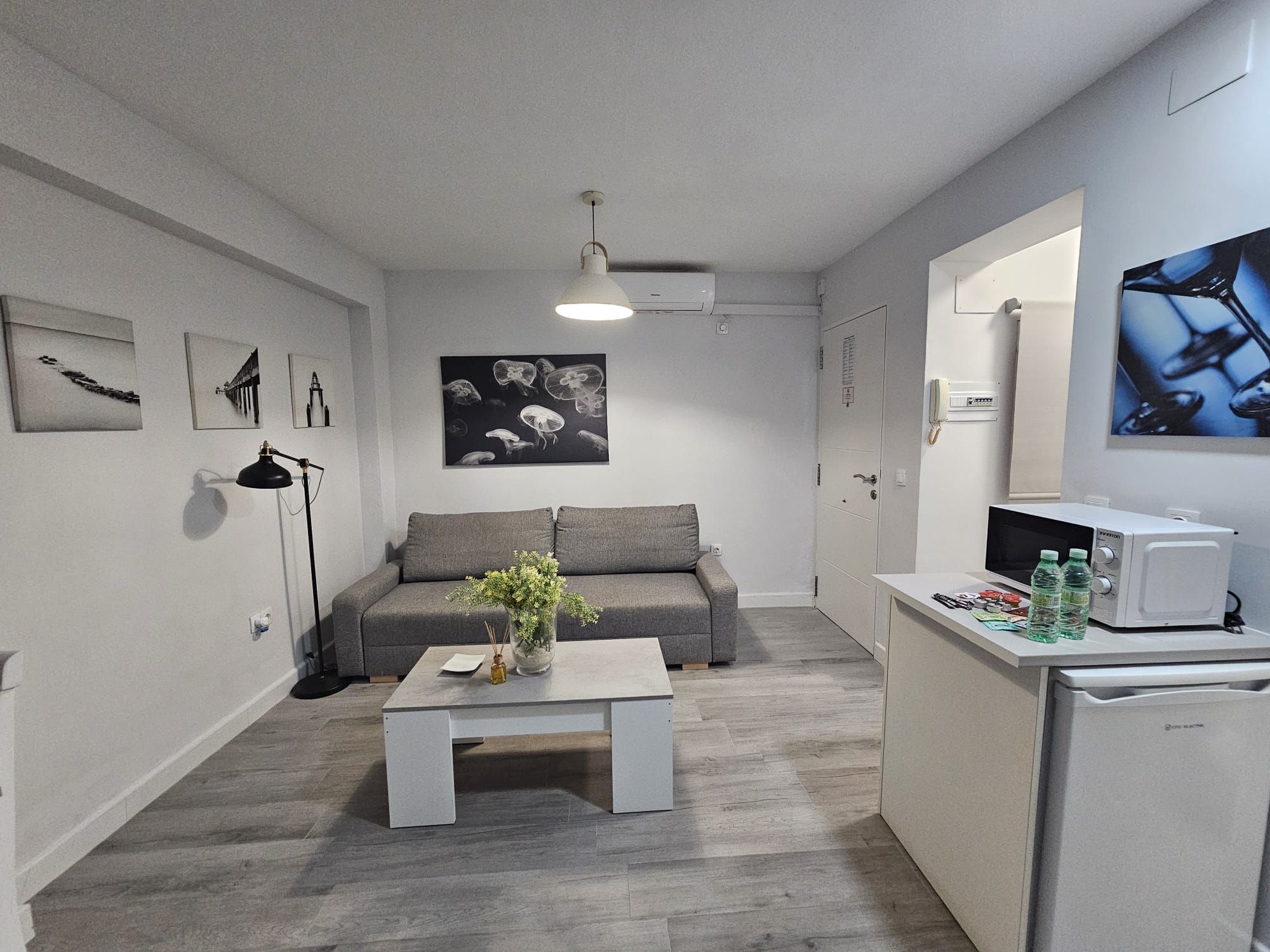 Un espacio habitable compacto con un sofá gris, una mesa de centro con un florero, un microondas y un refrigerador.