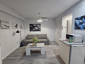 Un espacio habitable compacto con un sofá gris, una mesa de centro con un florero, un microondas y un refrigerador.