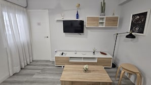 A modern living room with a flat-screen TV mounted on the wall, a wooden coffee table, a small side table, a floor lamp, and a minimalist decor style. - Puertas de la Catedral (Córdoba)