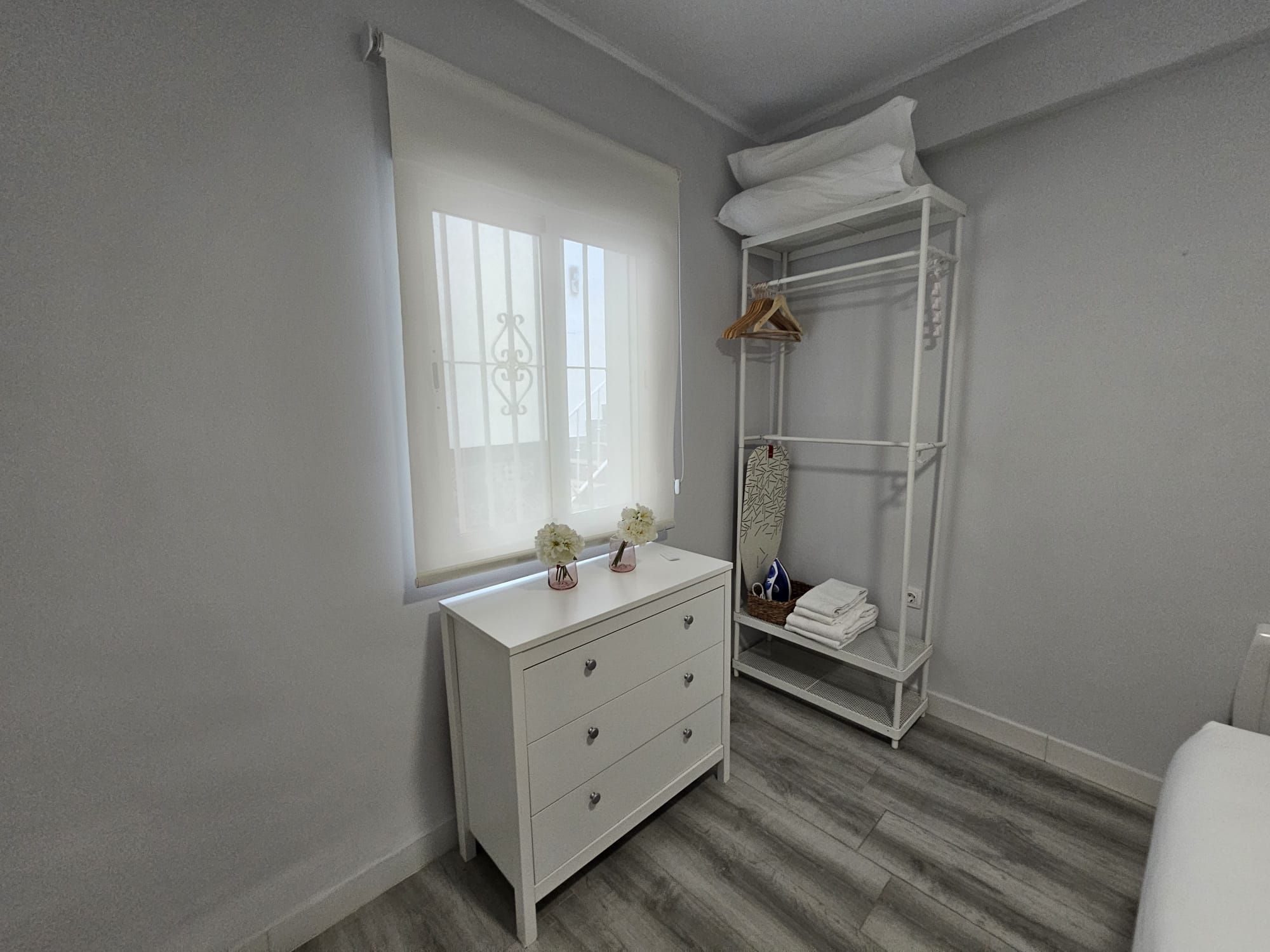 Een slaapkamer met een witte ladekast, een hangkast en een raam met jaloezieën.