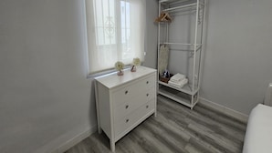A bedroom with a white dresser, a hanging wardrobe, and a window with blinds. - Puertas de la Catedral (Córdoba)