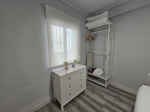 Un dormitorio con un aparador blanco, un armario ropero y una ventana con persianas.