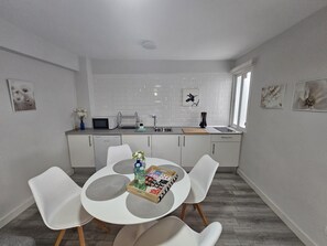 Een moderne keuken met witte kastjes, een eettafel met stoelen en een raam dat voor natuurlijk licht zorgt.