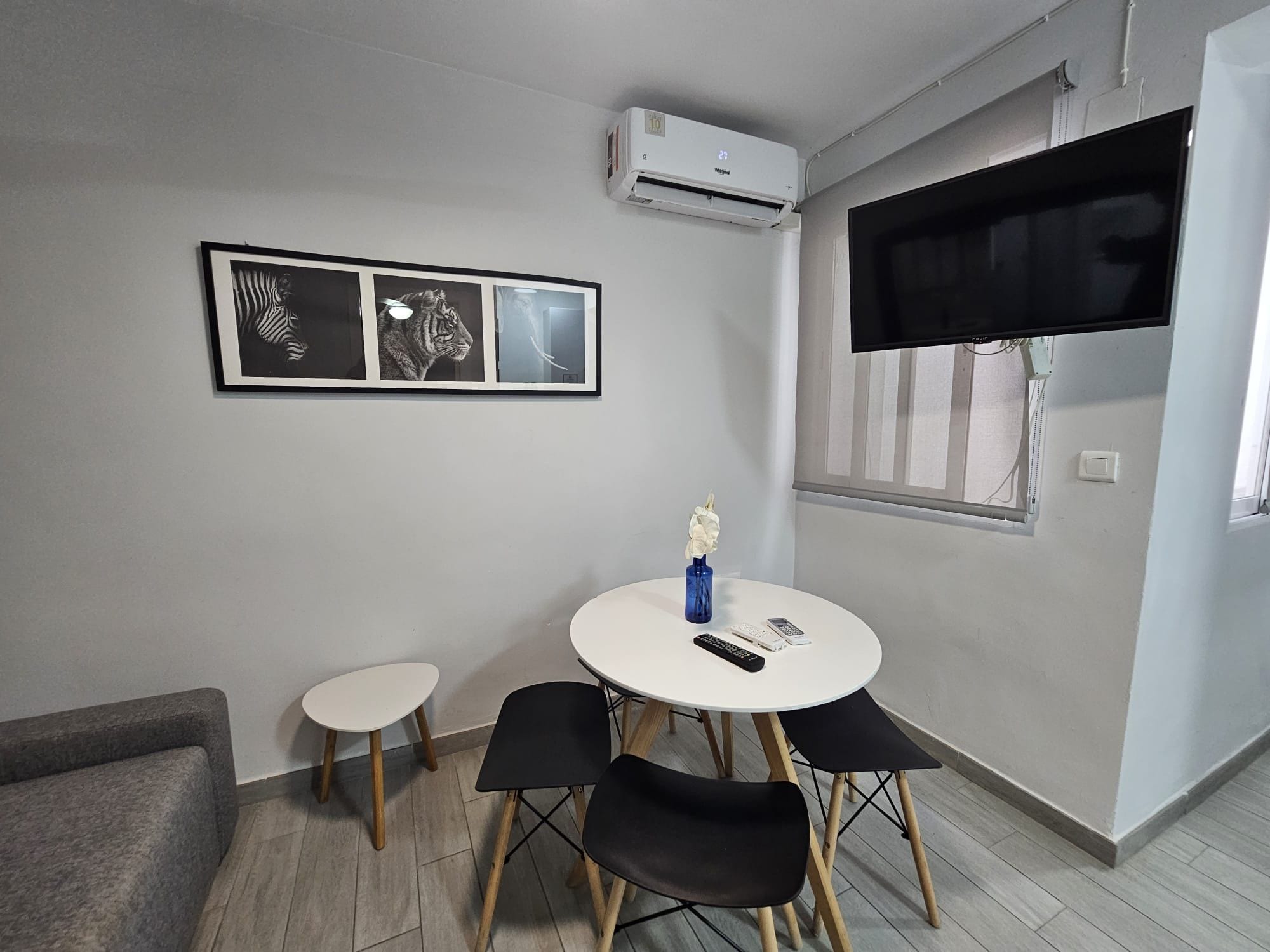 Una habitación pequeña y moderna con una mesa redonda, dos sillas, un televisor montado y obras de arte enmarcadas en la pared.