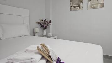 Un lit bien fait, avec des serviettes blanches pliées et un objet violet posé sur le côté.