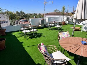 Een terras op het dak met kunstgras, tuinmeubilair en een schotelantenne.