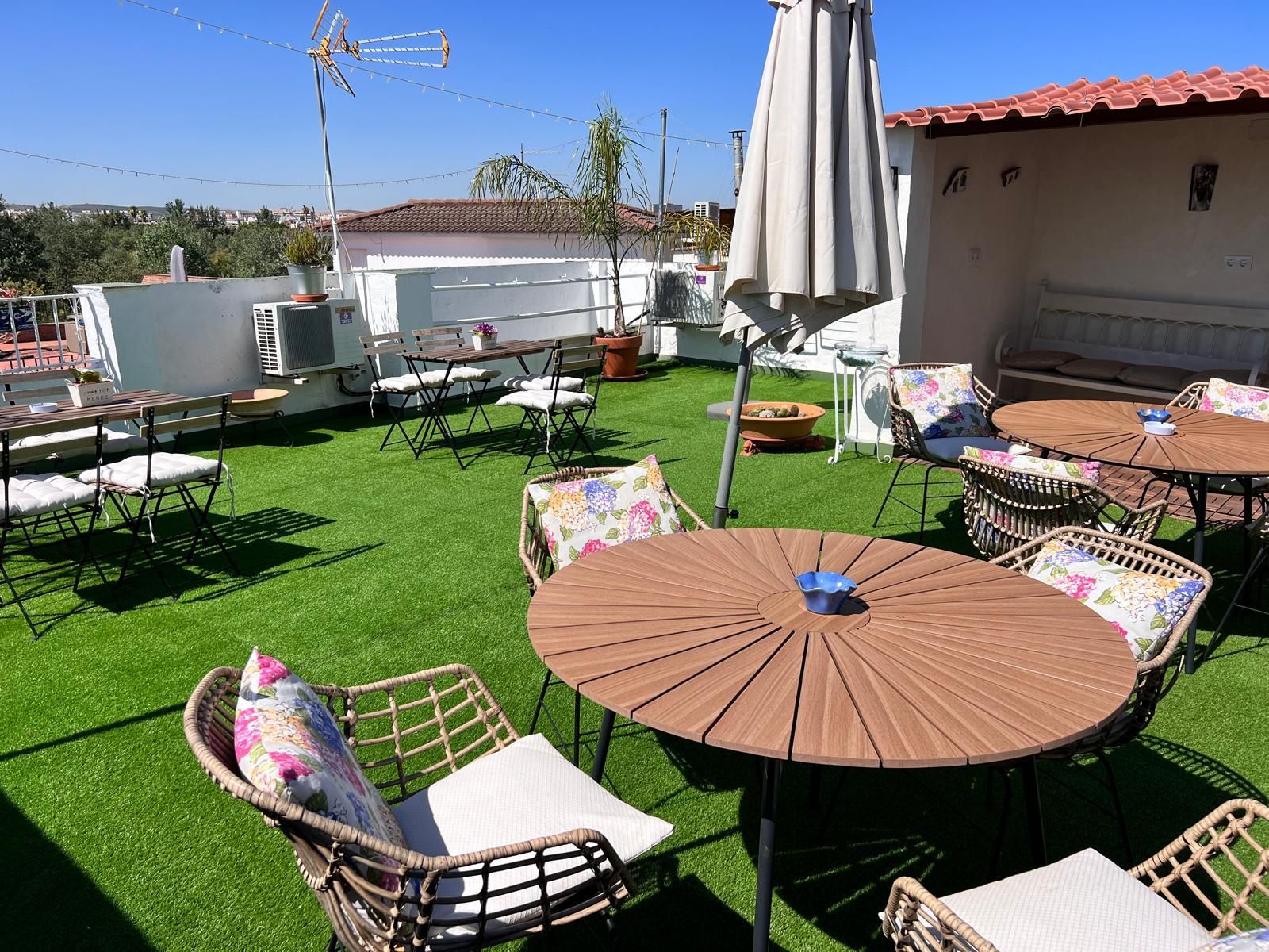 Un patio al aire libre con mesas redondas y sillas de mimbre, rodeado de césped artificial.
