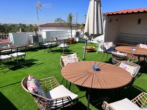 Un patio al aire libre con mesas redondas y sillas de mimbre, rodeado de césped artificial.