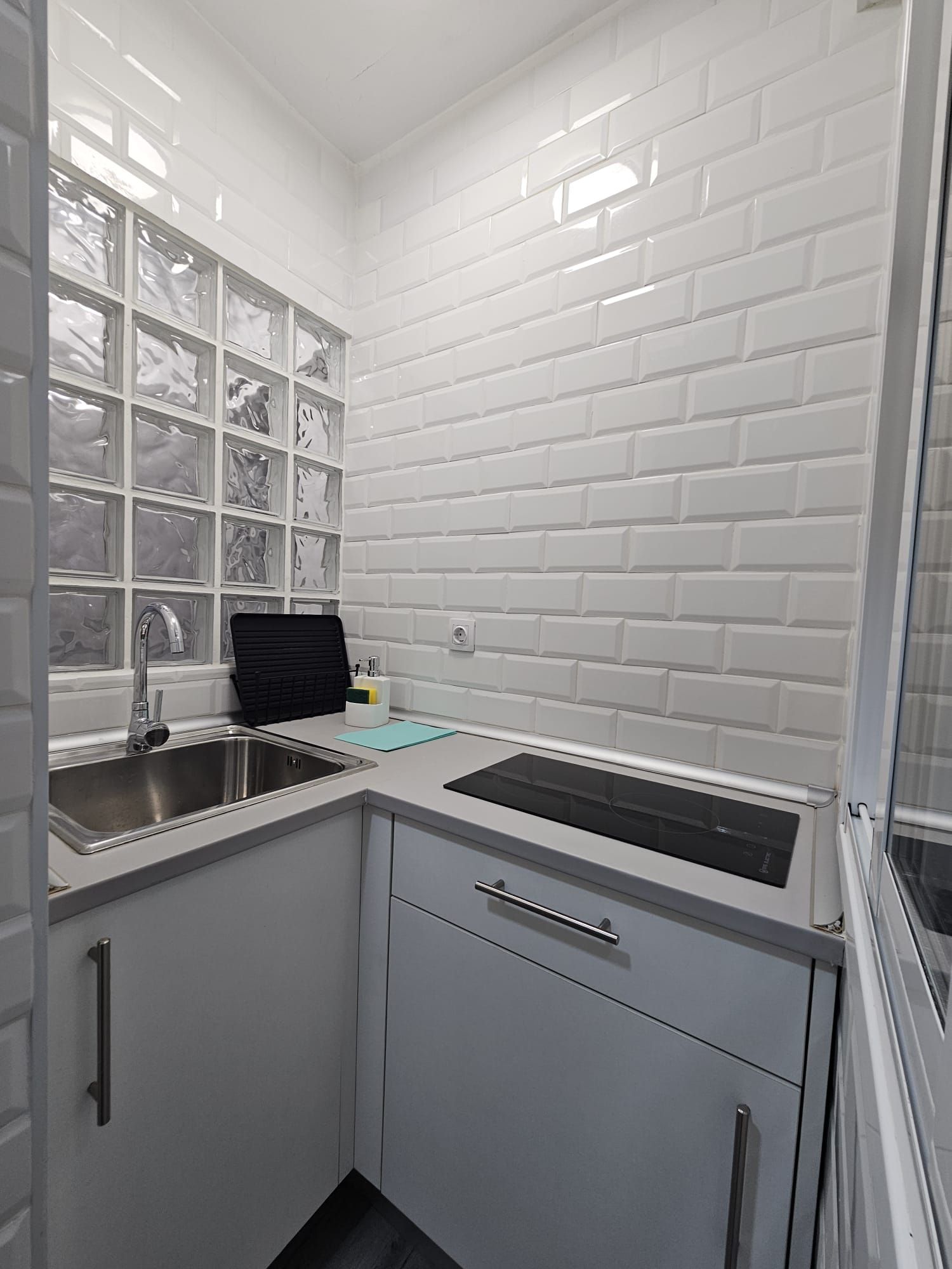 Une cuisine compacte avec un dosseret de carrelage blanc rectangulaire, un évier en acier inoxydable et un plan de travail noir.