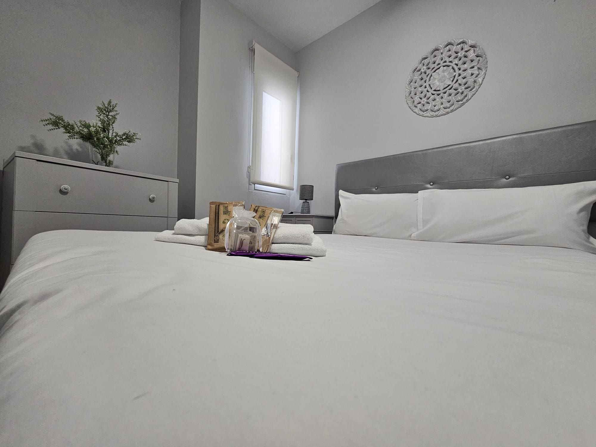 A neatly made bed with white linens, a decorative wall piece, and a window with curtains.