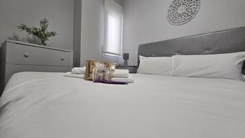 A neatly made bed with white linens, a decorative wall piece, and a window with curtains.