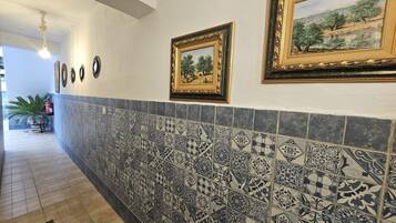 A hallway with patterned tiles, framed artwork on the walls, and a potted plant.