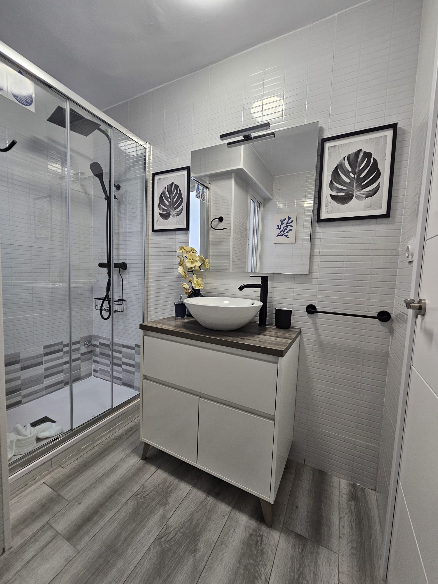 Un baño moderno con cabina de ducha de vidrio, un lavamanos blanco de gran tamaño y un mueble de tocador de madera.