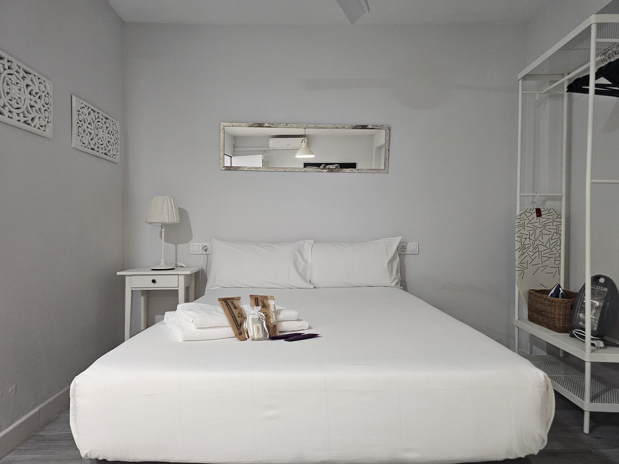 Una habitación de hotel con una cama, una mesita de noche, una lámpara, un espejo y un armario.