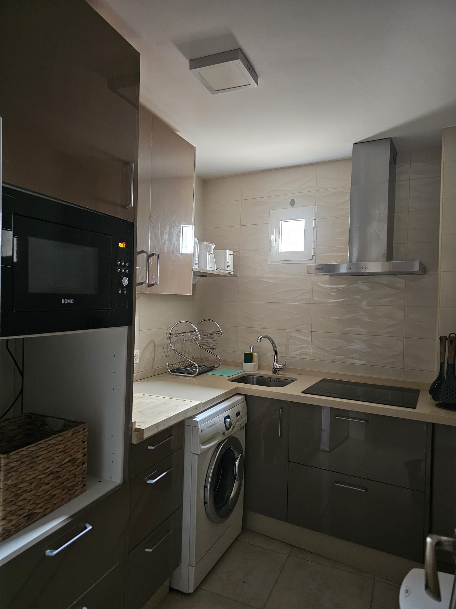 Uma cozinha compacta com micro-ondas embutido, máquina de lavar, pia e exaustor de aço inoxidável.
