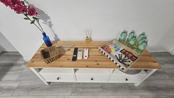 A wooden table with a vase, remote controls, a diffuser, and a tray of snacks and drinks.