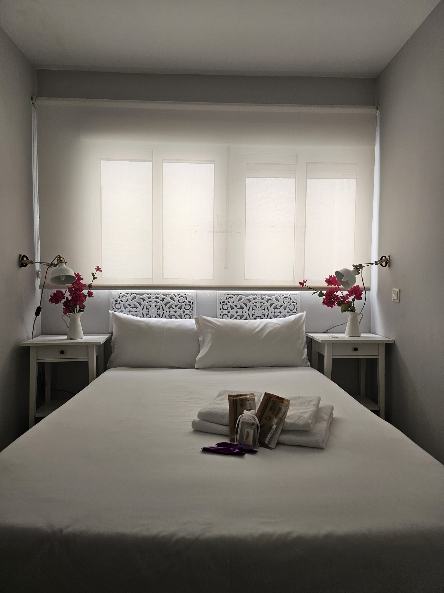 Une chambre d’hôtel avec un grand lit, deux tables de chevet, une tête de lit décorative et une fenêtre avec des rideaux.