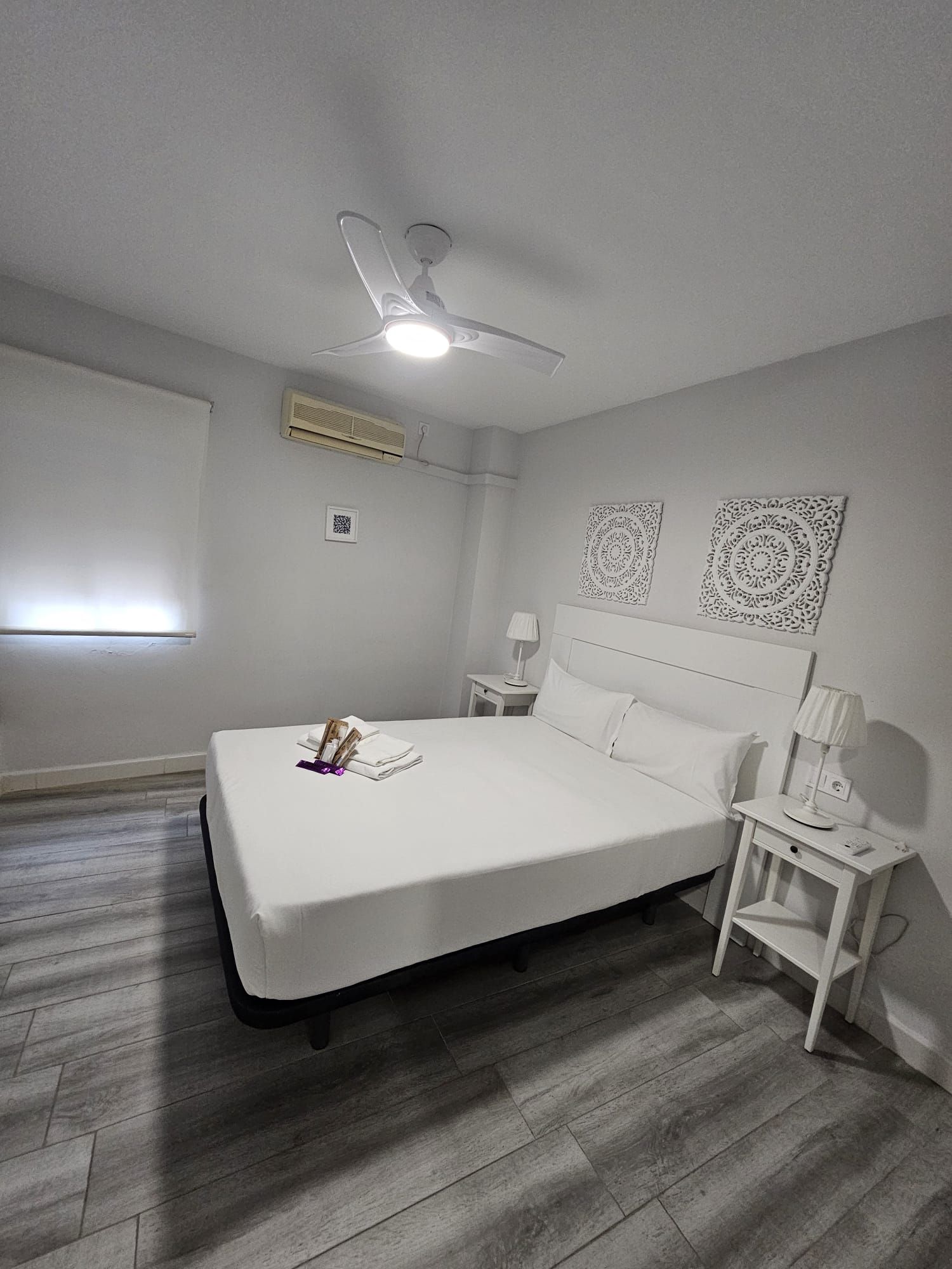A bedroom with a bed, a nightstand, a lamp, a ceiling fan, and decorative wall art.