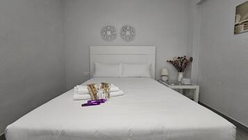 Una cama bien hecha con almohadas y una pequeña bolsa, una mesita de noche con una lámpara y un florero, y una pared con dos diseños circulares decorativos.