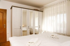 Ein Hotelzimmer mit einem Bett, einem Schrank mit Spiegeln und einem Fenster mit durchsichtigen Vorhängen.