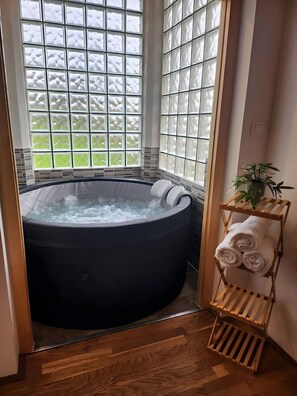 Ein Whirlpool in einem Raum mit großen Fenstern, Holzboden und einem Handtuchhalter mit Handtüchern.