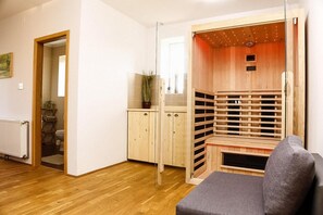 A room with a sauna, wooden cabinets, a radiator, and a grey sofa. - Holiday Home 'Lukovdol' with Hot Tub and Sauna (Lukovdol)