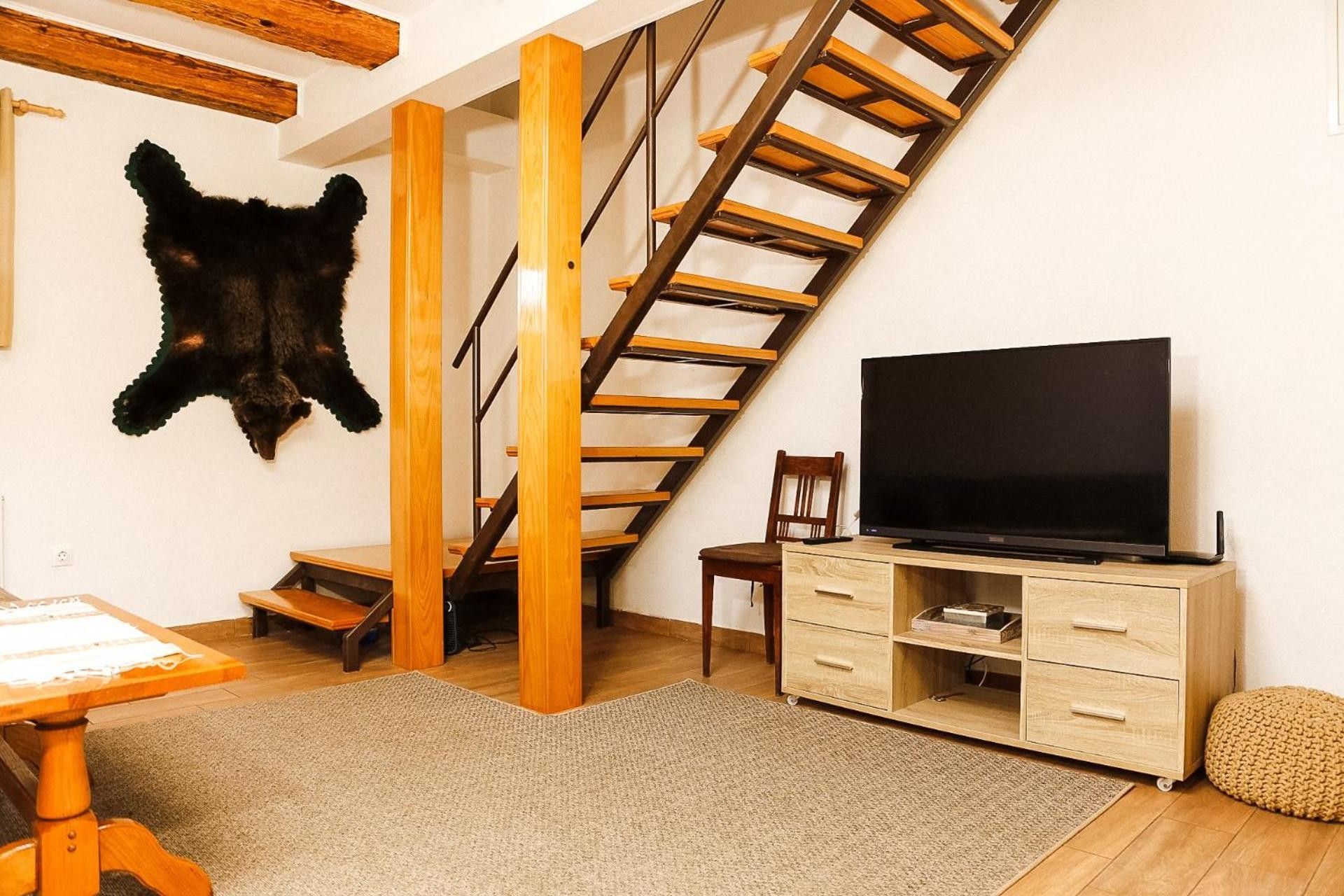 A room with a wooden staircase, a television on a wooden cabinet, and a leather hide on the wall.