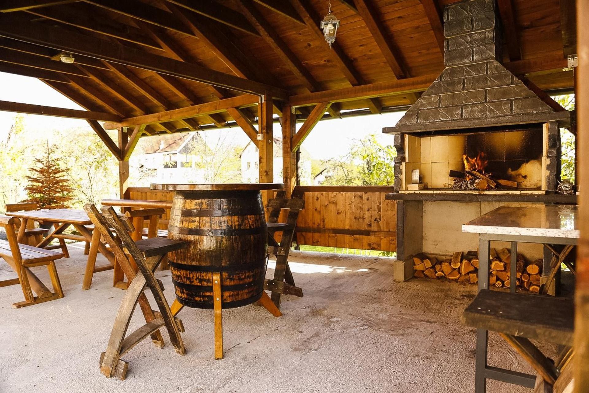 Een houten constructie buiten, met een stenen schoorsteen, picknicktafels en een vat.