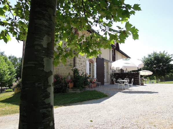 A stone building with a gravel driveway, outdoor seating, and a tree in the foreground.