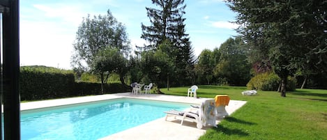 A swimming pool with lounge chairs and a table, surrounded by a well-maintained lawn and trees.