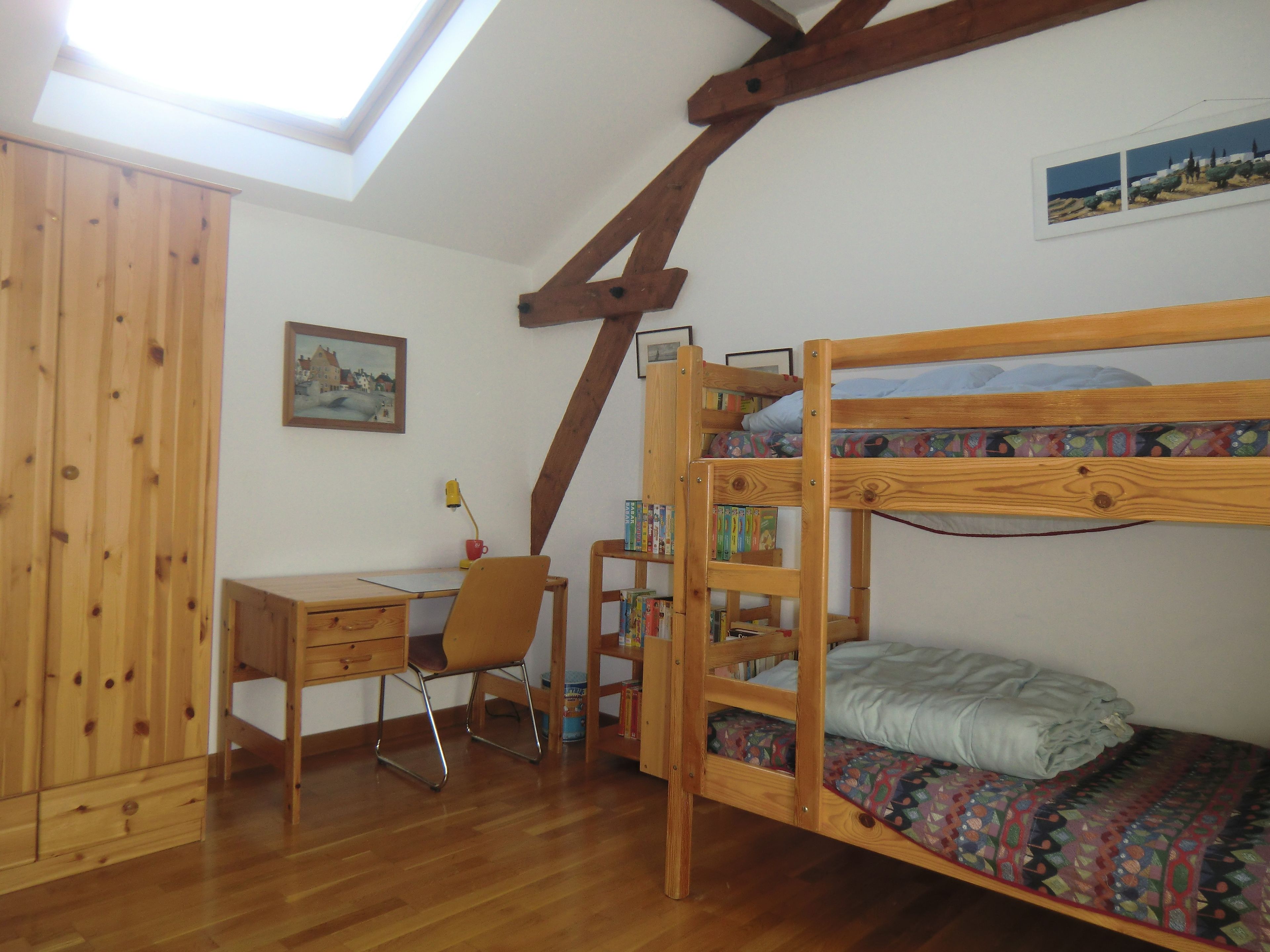 Ein Zimmer mit einem Etagenbett, einem Schreibtisch, einem Stuhl und einem Bücherregal.