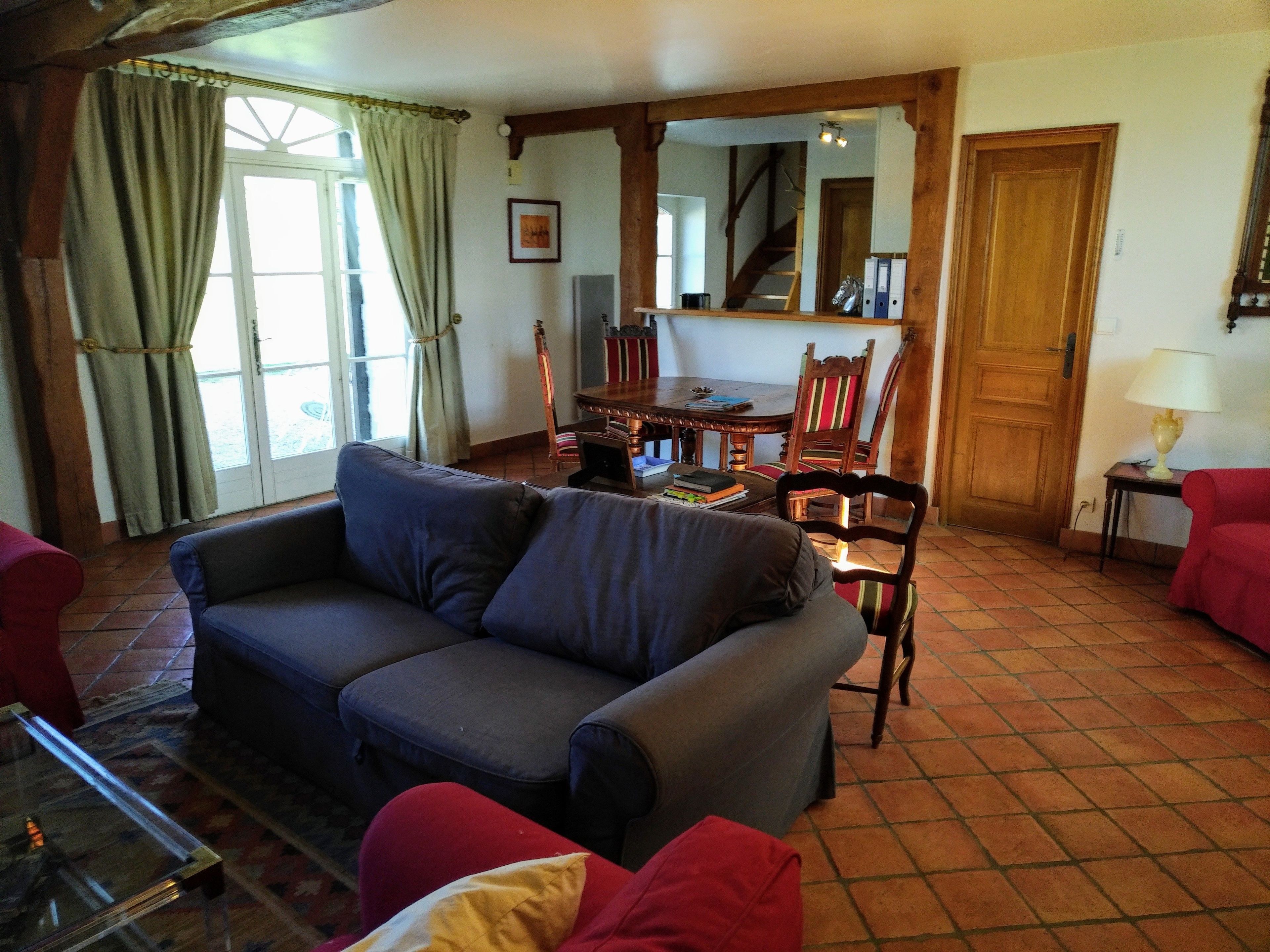 Een woonkamer met een bank, een eettafel met stoelen, een trap en een deur.